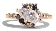 an oval cut diamond surrounded by blue and white diamonds in a yellow gold band ring