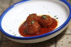 two meatballs covered in marinara sauce on a white and blue rimmed plate