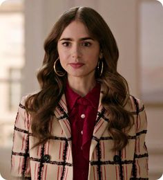 a woman with long brown hair wearing a red shirt and plaid coat, standing in front of a building