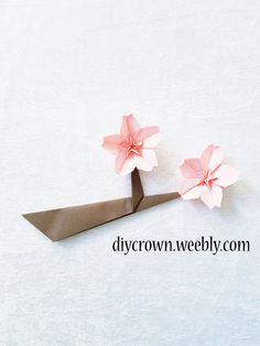 two pink paper flowers sitting on top of a pair of scissors