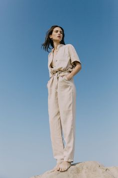 a woman standing on top of a sand dune with her hands in her pockets and looking off into the distance