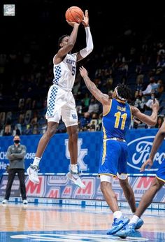 two men are playing basketball in front of an audience at a sporting event, one is jumping up for the ball