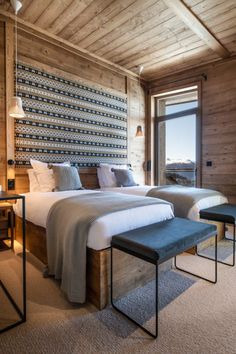 two beds in a room with wooden walls and floor to ceiling windows overlooking the mountains