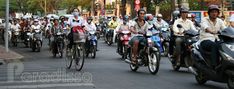 a large group of people riding motorcycles down the street in front of cars and motorcycles