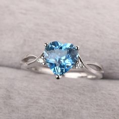 a heart shaped blue topazte and diamond ring on a white surface with a light gray background