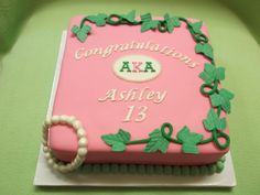 a pink cake decorated with green leaves and ribbons on a white plate that says congratulations aka astley 13