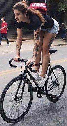 a woman riding a bike down the street with tattoos on her arm and leg,