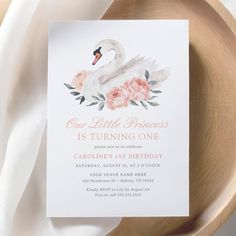 a white swan birthday party card with pink flowers and leaves on the front, sitting on a wooden plate