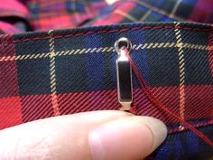 someone is stitching the side of a plaid shirt with a sewing needle on it