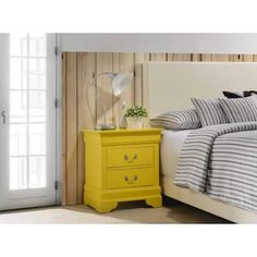 a bedroom with a yellow nightstand next to a bed and white door leading into the room