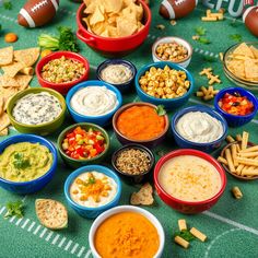 several bowls of dips, crackers, and vegetables on a football field table