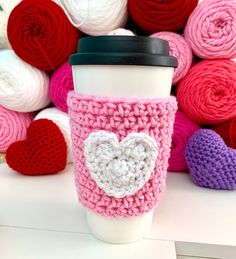 a coffee cup with a crocheted heart on it next to balls of yarn