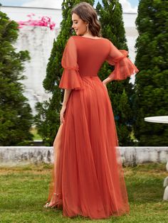 a woman in an orange dress standing on the grass with her back to the camera