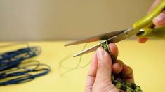 someone is cutting fabric with scissors on a yellow table top next to blue and green crochet