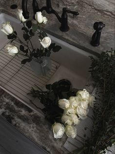 a bunch of white roses in a vase sitting on a kitchen sink counter top next to a faucet