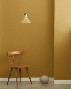 a wooden chair sitting in front of a wall with a light hanging from it's side