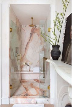 a bathroom with marble walls and flooring next to a bathtub, shower head, and vase