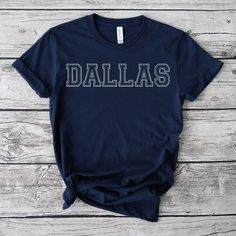 Dallas T-shirt, Dallas Shirt, Dallas Tee, Dallas Gift, Dallas Clothing, Dallas Trip, Dallas Vintage, Beautiful Dallas. PRODUCTION TIMELINE: 1-3 business days (Typically 2 days) DELIVERY TIMELINE: 2-5 business days (Usually 3 days) PRODUCT DETAILS: Bella Canvas Unisex T-shirt - Crafted from luxuriously soft cotton with a top-notch print quality. - Made with 100% soft cotton (fiber composition may vary for different colors) - Light fabric (4.2 oz/yd² or 142 g/m²) - Fits true to size Our Relaxed Fit Tee (Bella + Canvas style 3001) is a unisex design that runs slightly snug for men and a bit generous by about half a size for women. It is a relaxed fit and offers a plush, comfortable feel. * For T-shirt sizing, please consult the reference image in the listing. CARE GUIDE: Machine wash: warm (m Blue College T-shirt With Name Print, Collegiate T-shirt With Text Print In Relaxed Fit, Collegiate Text Print T-shirt With Relaxed Fit, Collegiate Relaxed Fit Text Print T-shirt, Collegiate Style Relaxed Fit T-shirt With Text Print, Casual Cotton Transfers With Text Print, Collegiate Cotton T-shirt With Name Print, Blue Tops With Name Print For College, College Team Name Relaxed Fit T-shirt