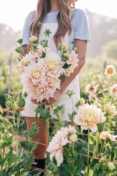 a woman holding a bouquet of flowers in front of her face while standing in a field