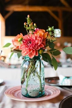 a mason jar filled with flowers sitting on top of a table next to plates and utensils