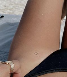 a woman is sitting on the beach with her cell phone in her hand and she's showing off her tiny tattoo