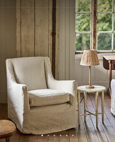 a living room with a chair, table and lamp next to an open window in the wall