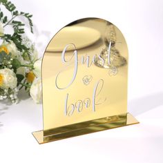 there is a gold book holder with flowers in front of it and the words guest on it