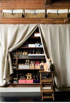 an open closet with shoes and other items on shelves in front of a curtained window