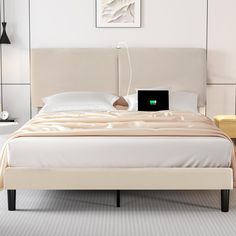 a bed with a laptop on top of it in a room that has white walls