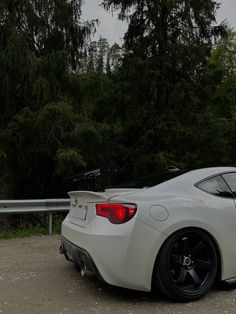 the rear end of a white sports car parked in a parking lot next to trees