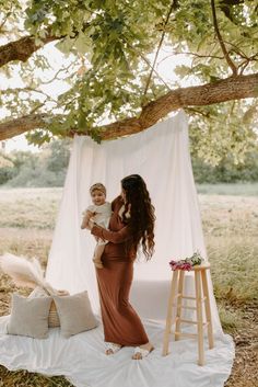 a woman holding a baby in her arms under a tree with a white drape