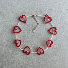 a red and white beaded heart bracelet on a white surface with a gold chain