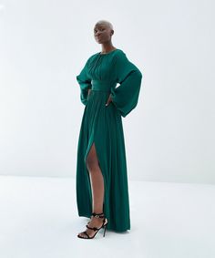 This stunning dress is made of a luxurious semi-satin fabric in a gorgeous emerald green color. It boasts a gathered neckline, wide waistband, and long gathered sleeves. The front-side slit adds a touch of elegance, and the soft rayon lining ensures maximum comfort. The back has a zip to the waist and a top covered button with minimal open slit for a chic look. Meet the Designer: The Baruni collection offers beautiful silhouettes and sophisticated fabrics as unique as you, for every occasion. Fa Gathered Neckline, Emerald Green Color, Gathered Sleeves, Wide Waistband, Event Dresses, Independent Designers Fashion, Stunning Dresses, Covered Buttons, Satin Fabric