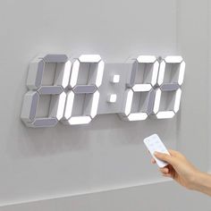 a person is holding a remote control in front of a digital clock on the wall