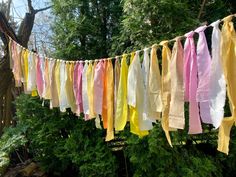 several different colored ribbons hanging from a line in front of some trees and shrubbery