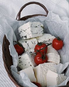 a basket filled with cheese and tomatoes on top of a white cloth covered tablecloth