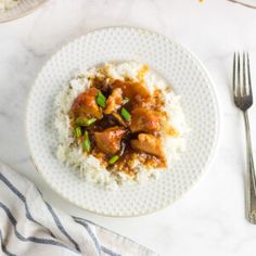 a white plate topped with chicken and rice next to a fork, knife and napkin