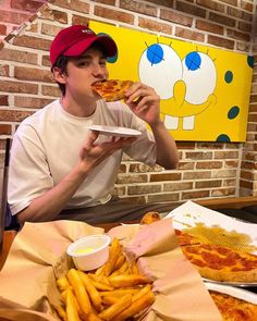 a man eating pizza and french fries in front of a spongebob painting on the wall