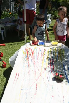 two children are standing at a table covered in paint