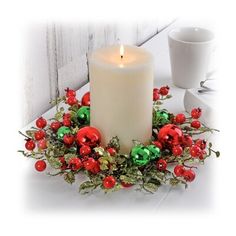 a lit candle surrounded by red and green christmas decorations on a white table next to a cup