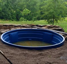 an empty blue swimming pool in the middle of a field with trees and grass behind it