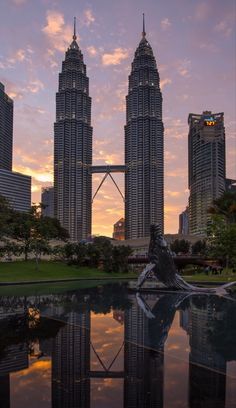 the reflection of two tall buildings in a body of water at sunset with skyscrapers in the background