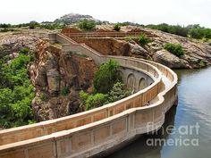 a man is standing on the edge of a bridge over water with cliffs in the background