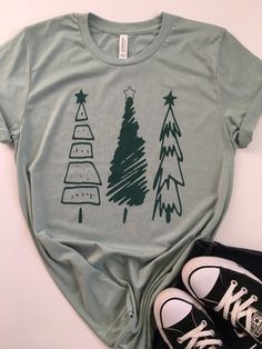 Christmas Shirt. Womens Christmas Shirt. Christmas Tree Tee. Christmas T-Shirt. Christmas Tees. Holiday Shirts. Christmas Graphic Tee. Everyone needs a favorite tee. This tee can be just that. This one has a cute tree design on a heather dusty blue colored tee with a dark green ink. It's soft, comfortable, and stylish. Grab one for yourself or your friend who loves Christmas! Christmas Tree Tee Bella/Canvas brand Unisex Fitted Tee, 4.2 oz 100% Combed and ringspun cotton The tee is heather dusty Christmas Cotton T-shirt, Christmas Graphic Print Short Sleeve Tops, Casual Green Christmas Shirt, Christmas Cotton Graphic Tee Shirt, Green Christmas Crew Neck T-shirt, Christmas Graphic Tee Shirt In Cotton, Green Christmas T-shirt For Holiday, Christmas Cotton Top With Graphic Print, Christmas Cotton Tops With Graphic Print