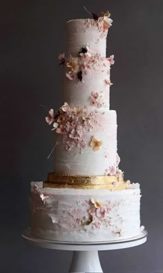 a three tiered white cake with pink flowers on top and gold trimmings