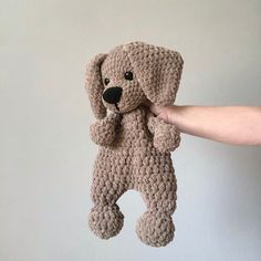 a person is holding up a crocheted stuffed dog in front of a white wall