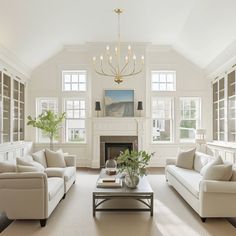 a living room filled with furniture and a fire place under a chandelier in front of two windows