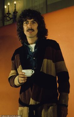 a man with long hair holding a cup in his hand and wearing a striped sweater