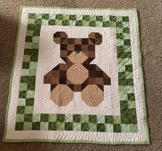 a teddy bear quilted on the floor with green and white checkerboard pattern