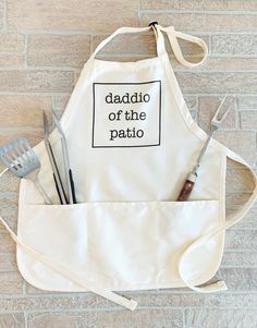 a white apron with the words daddio of the patio printed on it and utensils